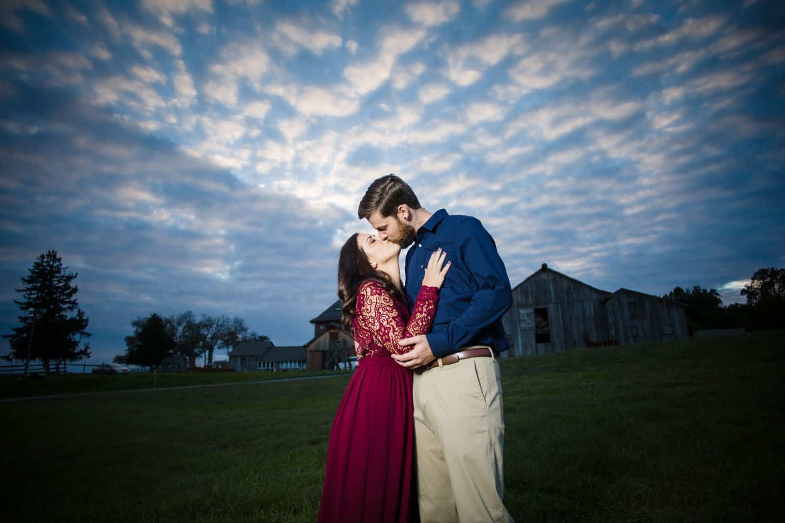 engagement session kissing with farm in the background