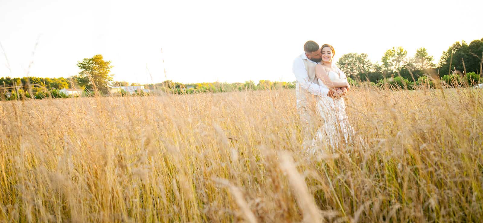 groom kisses bride on the neck from behind in tall grass field