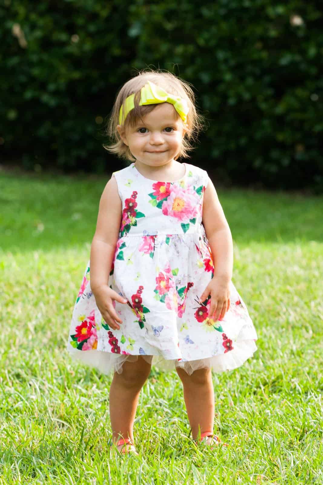 young girl in flower dress and yellow headband smiling