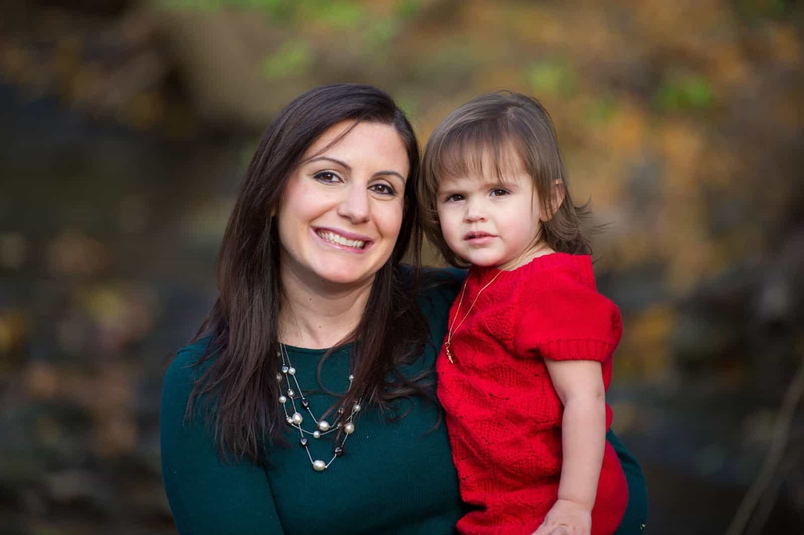 mother in green with daughter in red in front of trees