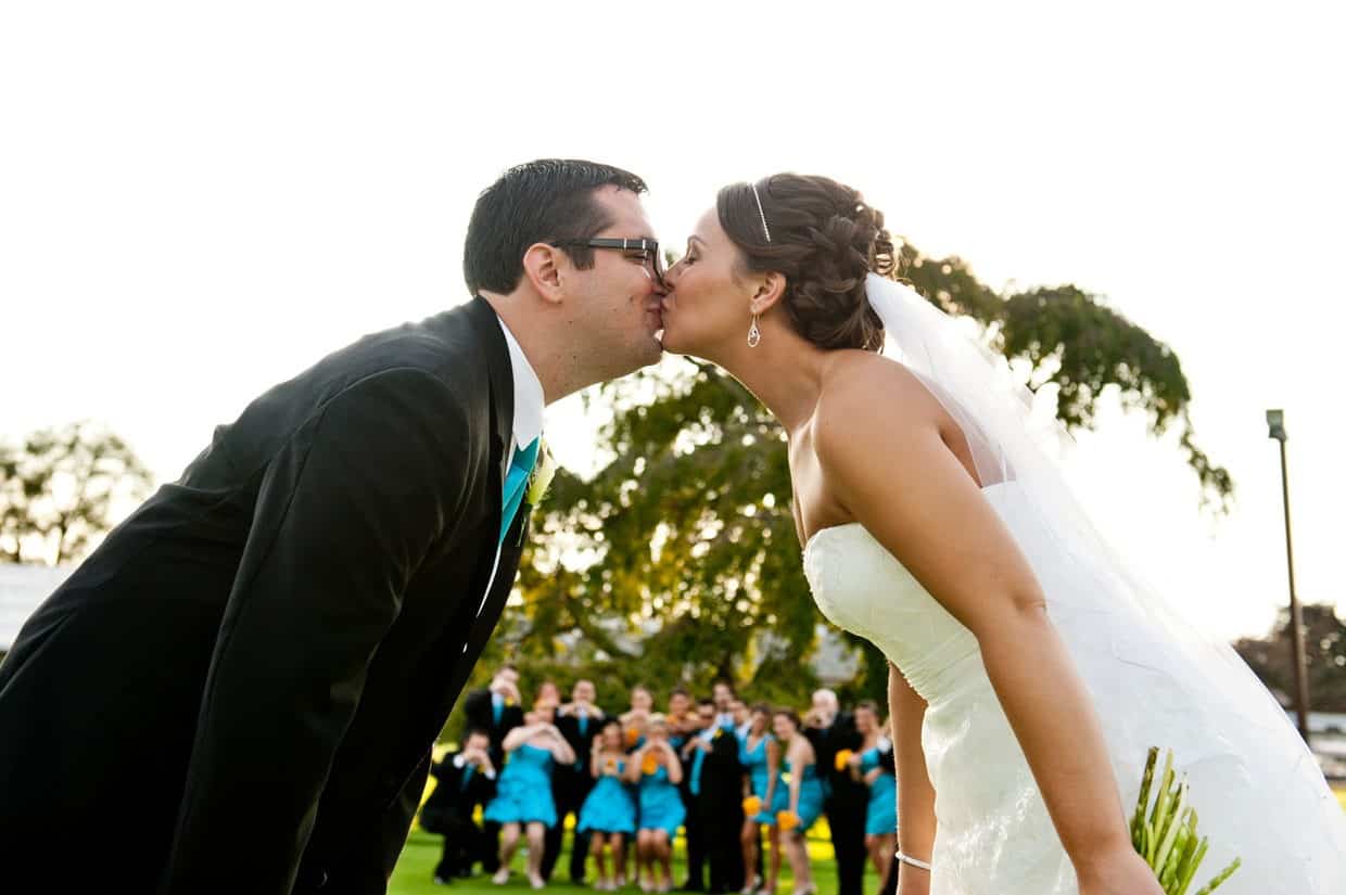 Kissing with bridal party behind at Penn Oaks Country Club